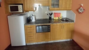 A compact kitchen with wooden cabinets, a microwave, a refrigerator, and a sink. - Casa da Fonte (Peso da Regua)