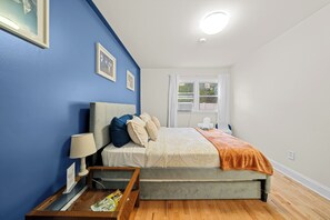 A bedroom with a bed, a nightstand, a lamp, a window, and a view of greenery outside. - Three bedrooms | Bright living room | Free parking (Jersey City)