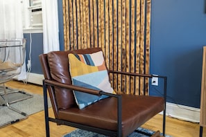 A brown leather chair with a colorful cushion, positioned in a room with a blue wall and a wooden slat backdrop. - Three bedrooms | Bright living room | Free parking (Jersey City)