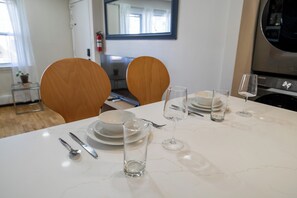 A dining table set with plates, cutlery, and glasses, with wooden chairs and a white marble table. - Three bedrooms | Bright living room | Free parking (Jersey City)
