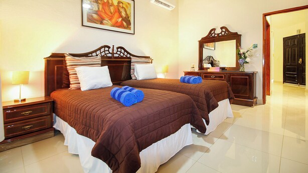 A hotel room with two beds, a wooden headboard, a nightstand with a lamp, a mirror, and a painting on the wall. - 4-Bedroom Villa with an Exclusive Private Pool, Sleeps 8 (playa del carmen)