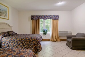Una habitación con una cama, una silla, un ventanal con cortinas y un equipo de aire acondicionado.