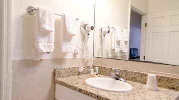 A bathroom with a granite countertop, a white sink, a mirror, and a towel rack with multiple towels.