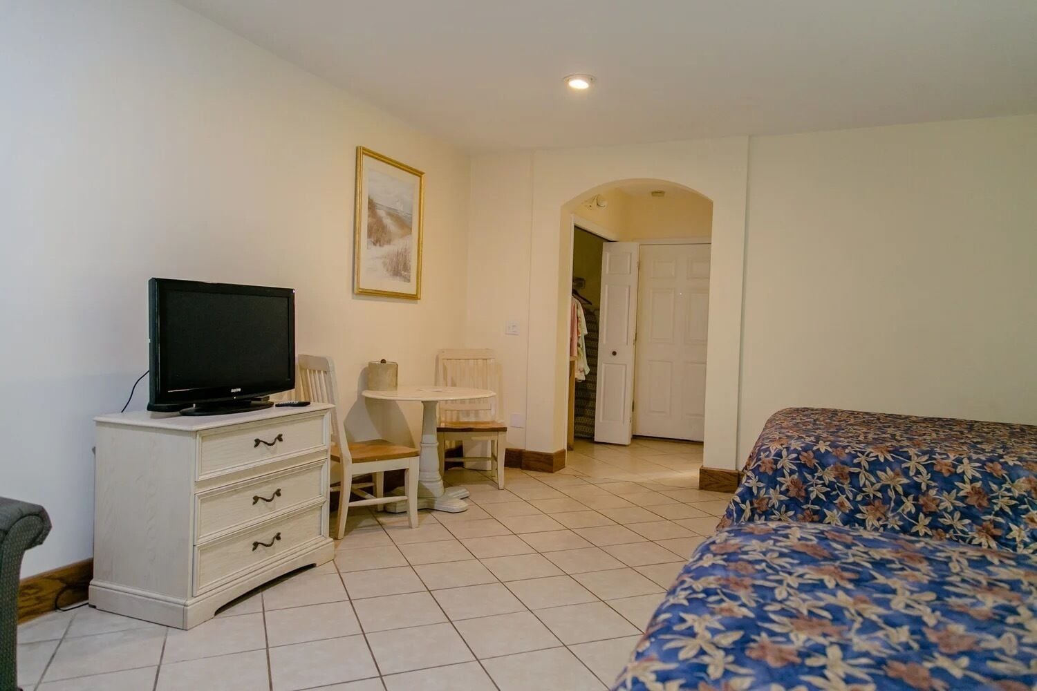 A hotel room with a bed, a television on a dresser, a small table, and a chair.