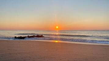 A beach with a sunset, waves, and a wooden structure.