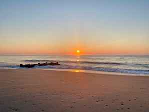 A beach with a sunset, waves, and a wooden structure.