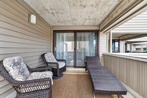 Ein Balkon mit Korbmöbeln, einer Schiebetür und Blick auf die Nachbarschaft.