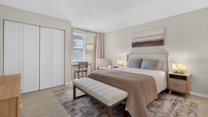 A bedroom with a bed, bedside tables, a bench, a chair, a wardrobe, and a window with blinds. - South Rehoboth | Ocean Block | Parking (Rehoboth Beach)