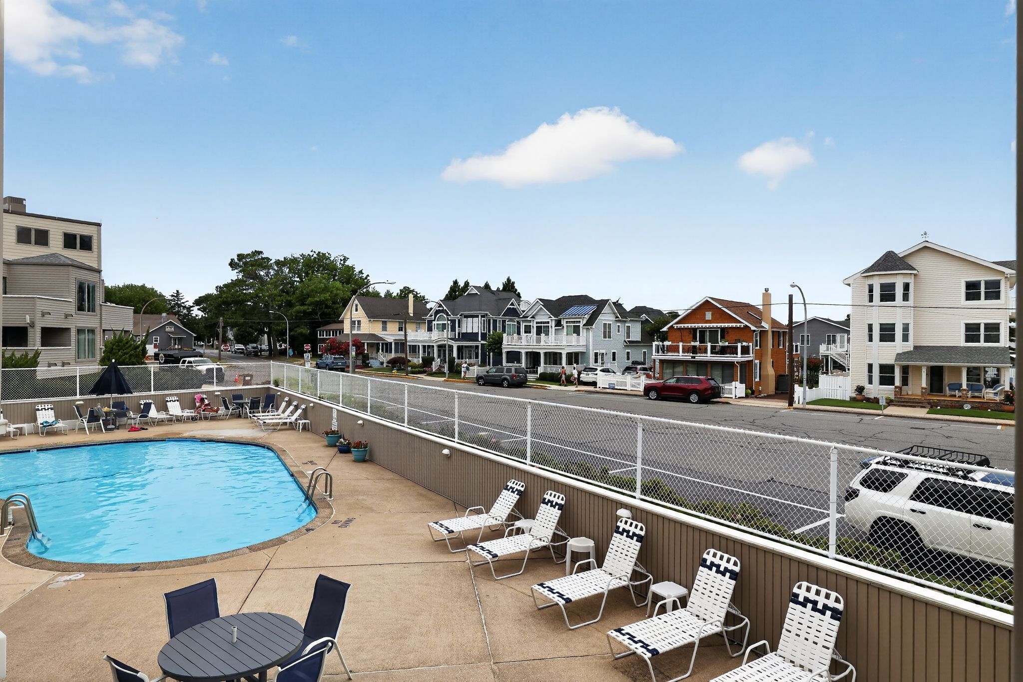 A swimming pool with lounge chairs and a view of a residential street.