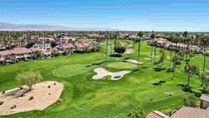 Un camp de golf amb búnquers de sorra, palmeres i edificis residencials al fons.