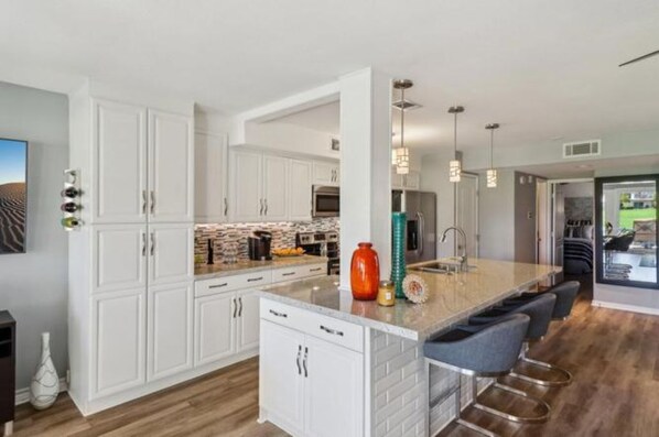 Cocina moderna con armarios blancos, una isla central con taburetes y luminarias colgantes.