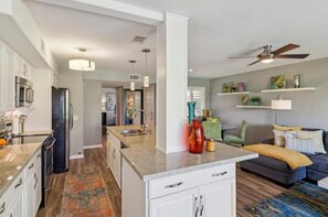 Een moderne keuken met een centraal eiland, een eetgedeelte met een bank en een woonkamer met plafondventilator.