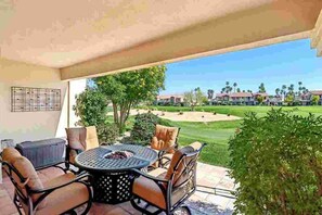 An outdoor patio with a round table and chairs, a fire pit, and a view of a golf course and residential buildings. - Remodeled 1-Bedroom on the Palm Royale Country Club Golf Course in La Quinta (La Quinta)