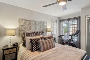 A bedroom with a bed, pillows, a nightstand, a ceiling fan, and a bicycle. - Remodeled 1-Bedroom on the Palm Royale Country Club Golf Course in La Quinta (La Quinta)