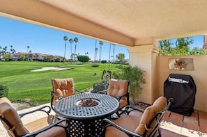 A patio with a round table and chairs, a grill, and a view of a golf course. - Remodeled 1-Bedroom on the Palm Royale Country Club Golf Course in La Quinta (La Quinta)