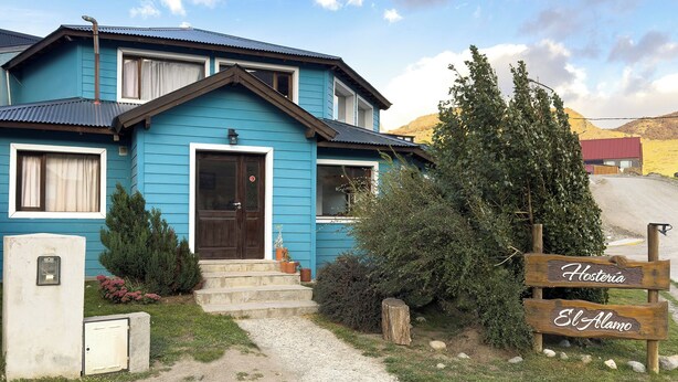 Una casa blu con un portone, un piccolo portico e un cartello che recita 'Hostería El Alamo'.