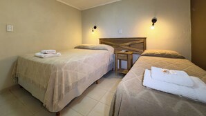Camera d'albergo con due letti, una testiera in legno, un tavolino e due luci a parete.