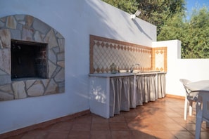 An outdoor kitchen area with a stone arch, tiled backsplash, and a table with chairs. - Villa Elaia - Country House with Private Pool (Siracusa)