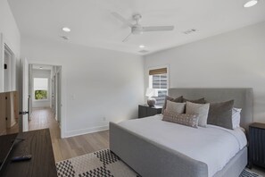 Un dormitorio con cama, ventilador de techo, mesita de noche, lámpara y vistas a un balcón.