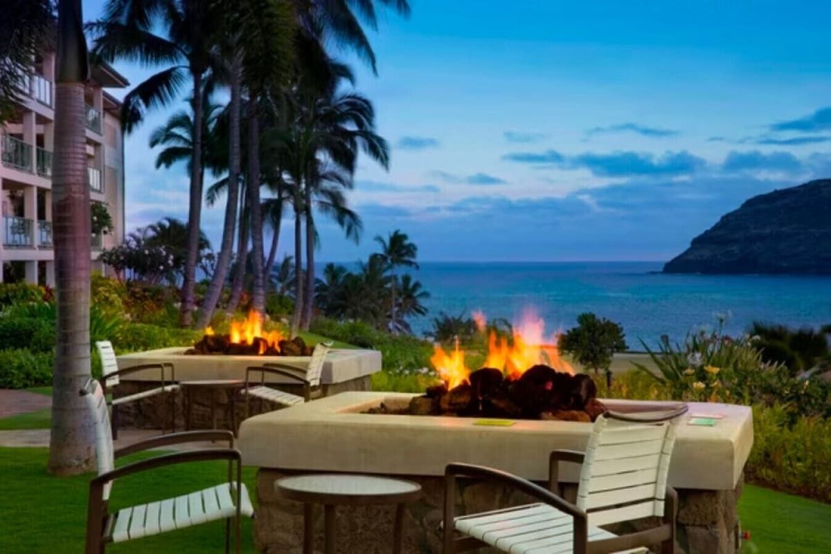 A beachfront patio with outdoor seating and a fire feature, overlooking the ocean.