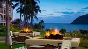 A beachfront patio with outdoor seating and a fire feature, overlooking the ocean.