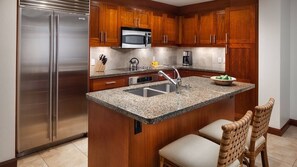 A kitchen with wooden cabinets, a stainless steel refrigerator, a microwave, a sink, and a granite countertop. - Luxury Ocean View Marriott's Kauai Lagoons - 2BR/2BA villa. Sleeps 6. (Lihue)