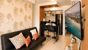 Ein Wohnzimmer mit einer schwarzen Couch, einem Fernseher, einer Holzkommode und einem Essbereich mit einem schwarzen Stuhl und Tisch.