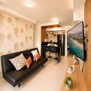 Ein Wohnzimmer mit einer schwarzen Couch, einem Fernseher, einer Holzkommode und einem Essbereich mit einem schwarzen Stuhl und Tisch.