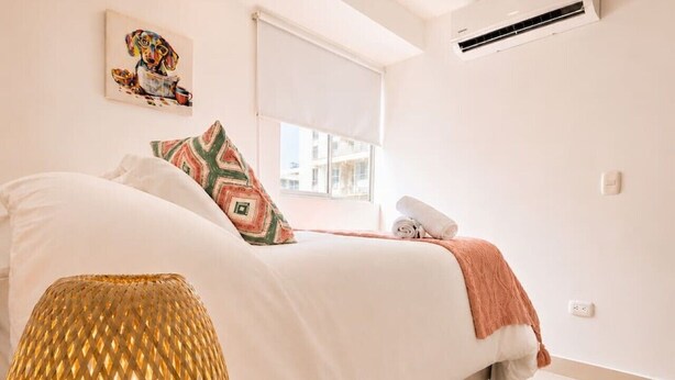 Ein Schlafzimmer mit Bett, Fenster, Klimaanlage und einer dekorativen Lampe.