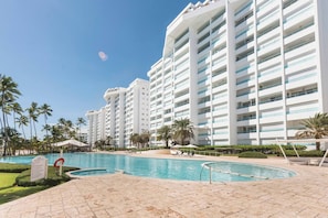 A resort with a swimming pool, palm trees, and a multi-story building with balconies. - Beachfront Apartment in Juan Dolio, Getaway Offer! (Playa Juan Dolio)