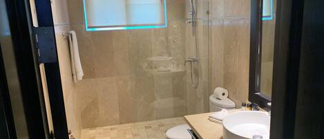 Un baño moderno con cabina de ducha de vidrio, inodoro, lavamanos con un espejo grande y un perchero para toallas.