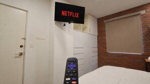 Un dormitori amb televisió penjada a la paret que mostra 'NETFLIX', un armari, un llit i una pared de maó.