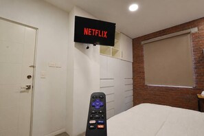 A bedroom with a TV mounted on the wall displaying 'NETFLIX,' a wardrobe, a bed, and a brick wall. - ¡Cerca de la Macroplaza! 6 personas, Alberca & Gym (Monterrey)