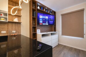 A modern living room with a flat-screen TV mounted on a wooden wall, a remote control on the counter, and a sliding door. - ¡Cerca de la Macroplaza! 6 personas, Alberca & Gym (Monterrey)