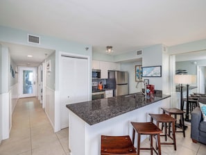A modern kitchen with a central island, bar stools, and a dining area with a lamp.