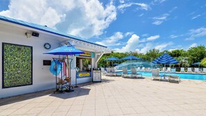 A poolside area with lounge chairs, umbrellas, a water feature, and a food service counter. - The Happy Reef 4209 King & Queen (Tavernier)