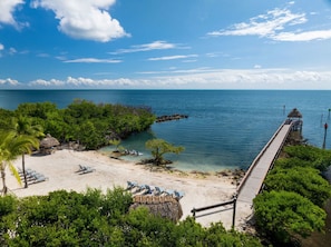 A beach with clear water, a wooden pier, and lounge chairs. - The Happy Reef 4209 King & Queen (Tavernier)