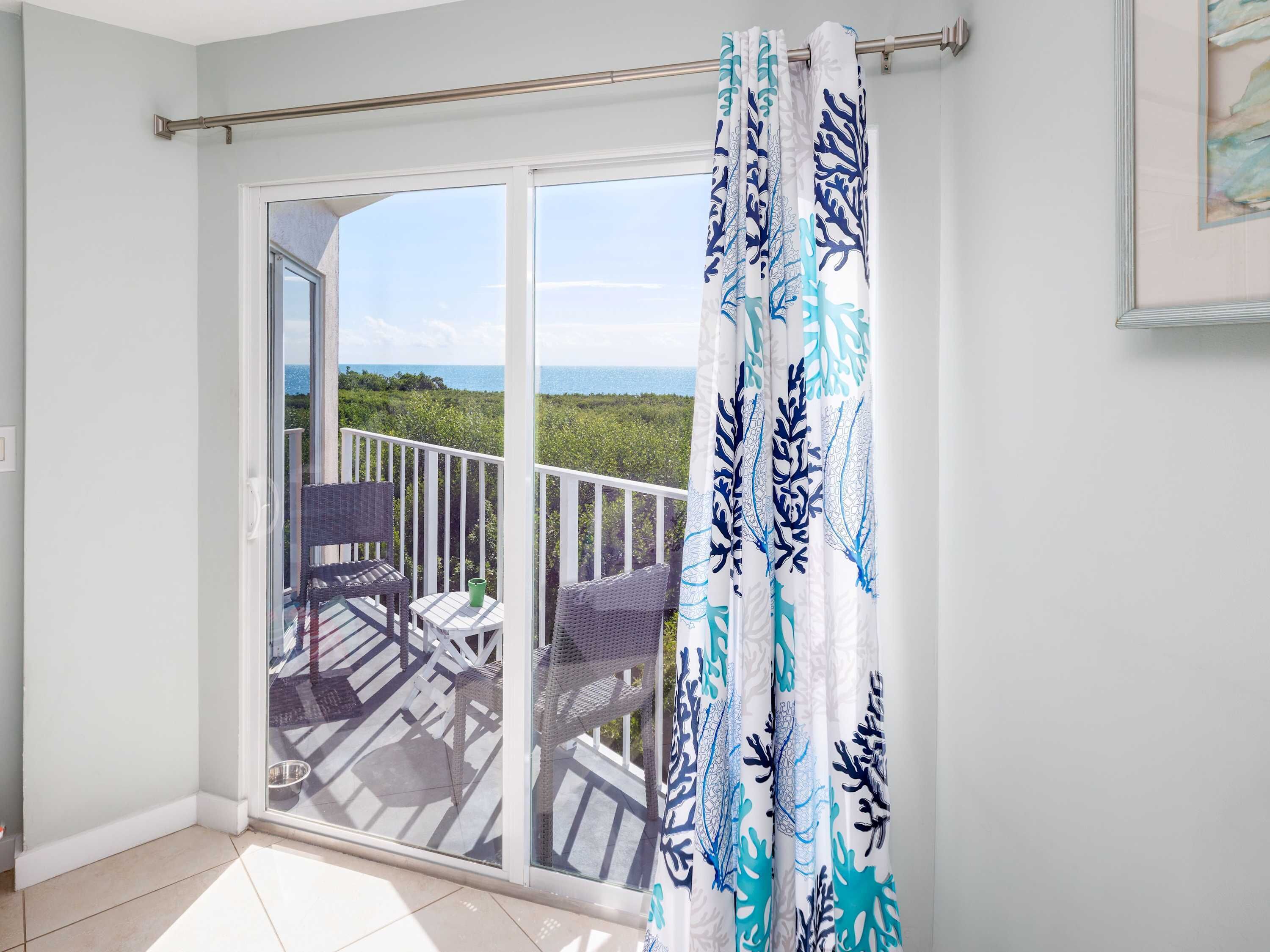 Een balkon met uitzicht op zee, een schuifpui en rieten meubilair.