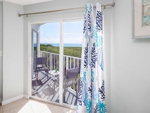 Un balcon avec vue sur la mer, une porte-fenêtre coulissante et des meubles en osier.