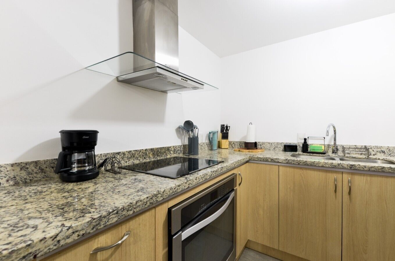 A kitchen with granite countertops, a stove, a coffee maker, a sink, and wooden cabinets.