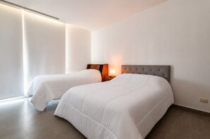 Ein Hotelzimmer mit zwei Betten, einem Nachttisch mit Lampe und einem großen Fenster mit Jalousien.