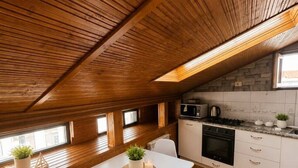 Une cuisine avec un plafond en bois, des armoires blanches, une table à manger avec des chaises et une petite fenêtre.