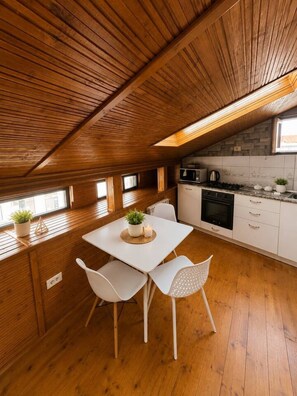 Eine Küche mit Holzbalkendecke, weißen Schränken, einem Esstisch mit Stühlen und einem kleinen Fenster.