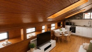 Un espace de vie moderne de style « loft », doté d’un plafond en bois, d’un coin cuisine et d’un espace salon avec un téléviseur et une table basse.