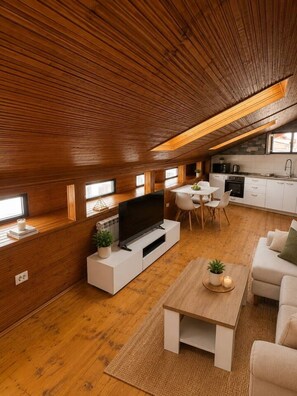 Ein stilvoller Loft-Wohnraum mit Holzbalkendecke, einer Küchenzeile und einer Sitzecke mit Fernseher und Couchtisch.