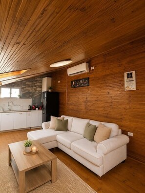 Ein gemütliches Wohnzimmer mit einer Eckcouch, einem Holztisch und einer Küchenzeile mit Kühlschrank und Herd.