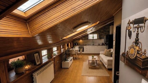 Un intérieur en bois avec un plafond en pente, un coin cuisine et un espace salon comprenant un canapé et une table basse.