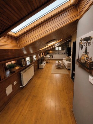 Un interno in legno con soffitto spiovente, una zona cucina e un’area salotto con divano e tavolino.