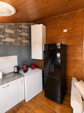 Una cocina compacta con un refrigerador negro, un gabinete blanco, un salpicadero de pared de piedra y un techo de madera.
