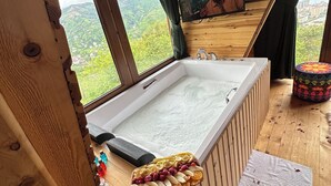 Una cabaña de madera con una bañera grande, un waffle y una ventana con vista a follaje.